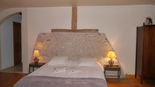 A cozy bedroom with a rustic stone headboard, warm lighting from bedside lamps, and wooden furnishings evokes a serene and inviting atmosphere, ideal for travelers seeking a tranquil retreat in a charming countryside setting.