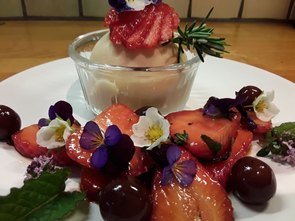 A beautifully plated dessert featuring strawberries, edible flowers, and a creamy mousse in a glass bowl creates an inviting and elegant dining experience perfect for a romantic getaway or gourmet food tour.