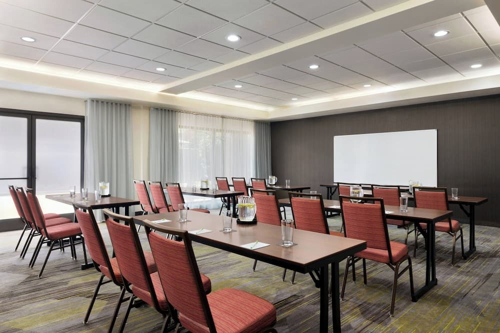 A modern conference room with rows of tables and red chairs set against large windows and a whiteboard, ideal for professional meetings and workshops.