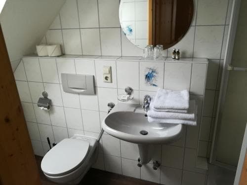 A cozy, compact bathroom with white tiled walls, a round mirror, and neatly folded towels offers a practical space for travelers seeking cleanliness and simplicity in their accommodations.