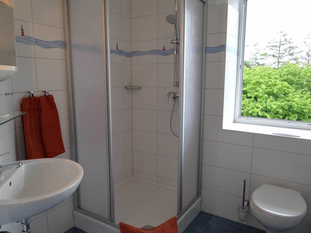 A bright, modern bathroom with a walk-in shower, nautical-themed tiles, and a window overlooking lush greenery, ideal for travelers seeking comfort and cleanliness in their accommodations.