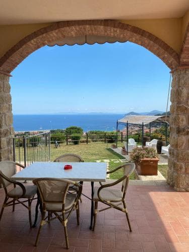 A serene coastal patio framed by an arched stone entryway offers a breathtaking view of the sea and distant hills, perfect for travelers seeking relaxation and scenic beauty.
