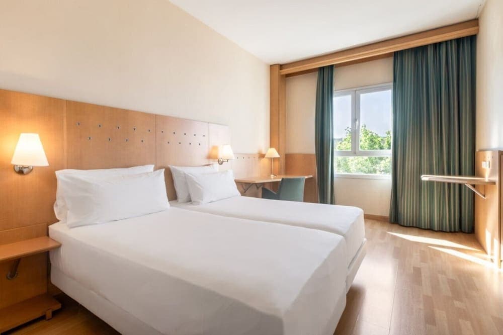 A cozy hotel room with two neatly made beds, wooden furnishings, soft lighting, and a window view of greenery, ideal for travelers seeking comfort and relaxation.