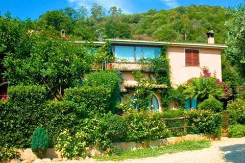 A charming, ivy-covered villa nestled among lush greenery and hills offers a serene retreat, ideal for travelers seeking a peaceful countryside escape.