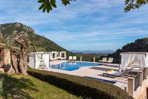 A serene luxury villa poolside scene with lounge chairs, olive trees, and breathtaking mountain views, ideal for a tranquil getaway in a Mediterranean setting.