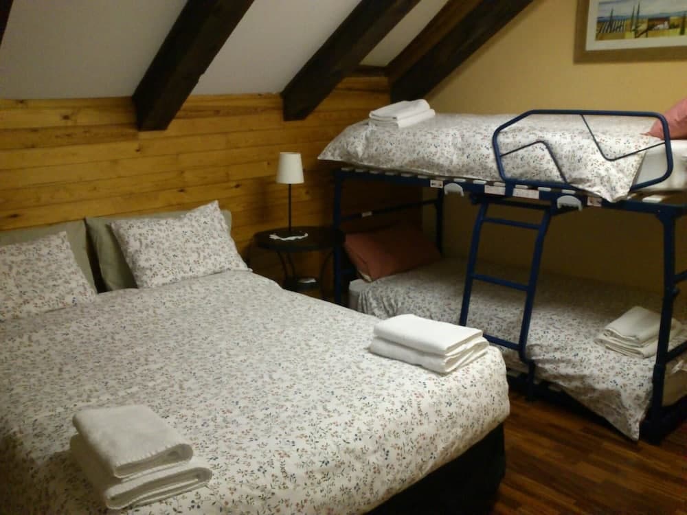 A cozy attic bedroom with wooden beams, floral bedding, bunk beds, and neatly folded towels offers a charming and budget-friendly accommodation option for travelers seeking a rustic retreat.