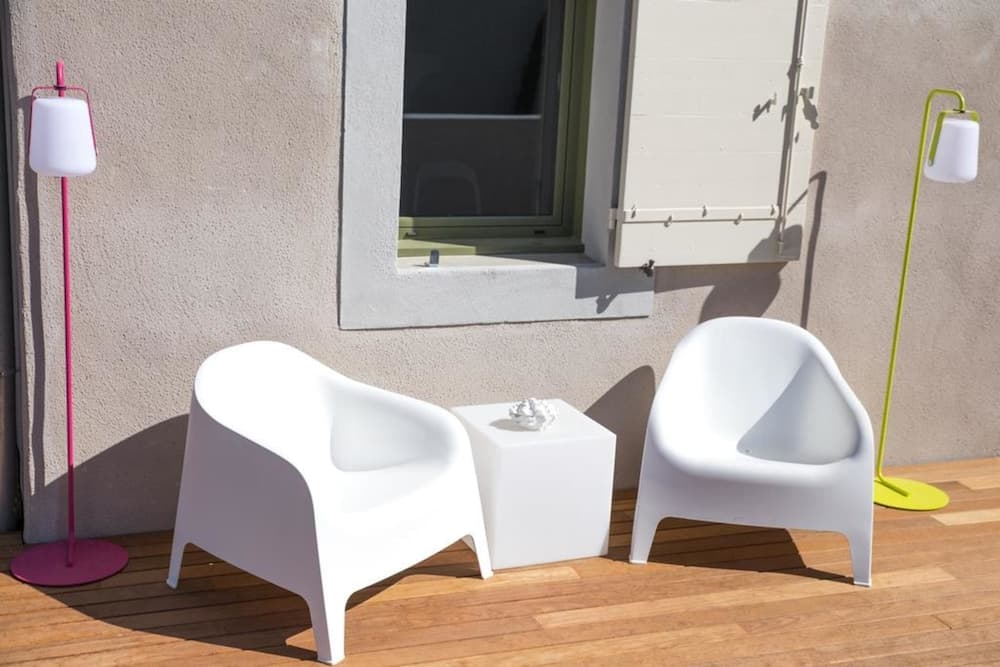 A cozy outdoor patio features sleek white chairs and a small table flanked by colorful standing lamps, creating a modern and inviting atmosphere perfect for relaxing or entertaining guests.