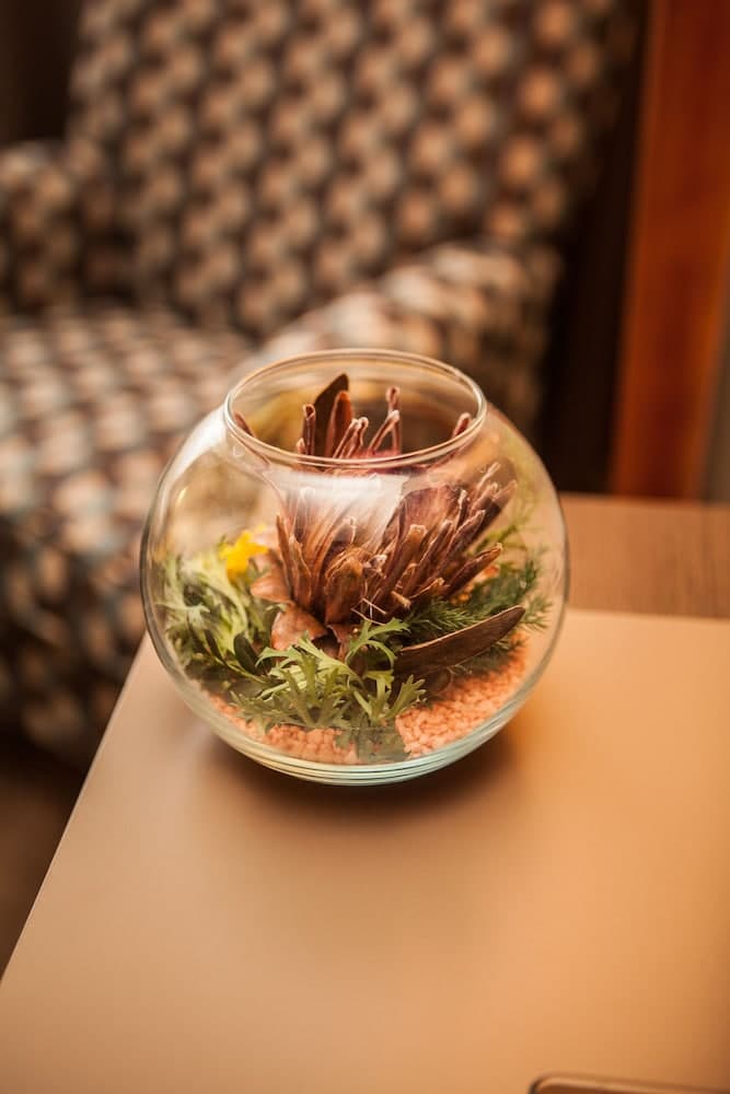 A cozy indoor setting features a glass terrarium with dried flowers and greenery on a beige table, creating a serene atmosphere ideal for relaxation or as a decorative element in a tranquil retreat.