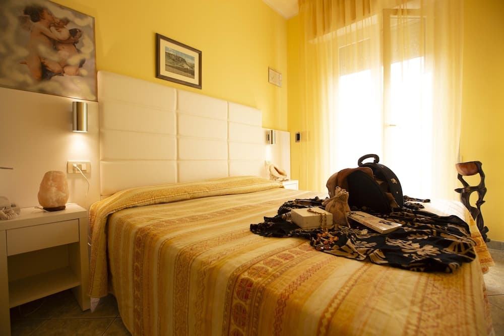 A cozy hotel room with yellow walls, a neatly made bed adorned with travel essentials, soft lighting from bedside lamps, and a serene atmosphere ideal for relaxation during a trip.