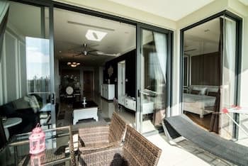 A cozy indoor-outdoor living space with sleek furniture, large glass doors, and a balcony featuring wicker chairs and loungers, ideal for a relaxing vacation retreat.