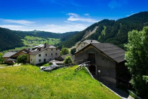 A serene mountain village with rustic wooden houses nestled among lush green hills under a clear blue sky, ideal for tranquil alpine retreats and nature photography.