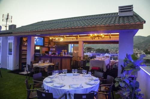 A cozy rooftop bar with a tiled roof and ambient lighting offers an intimate dining experience with scenic views, perfect for travelers seeking a romantic evening out.