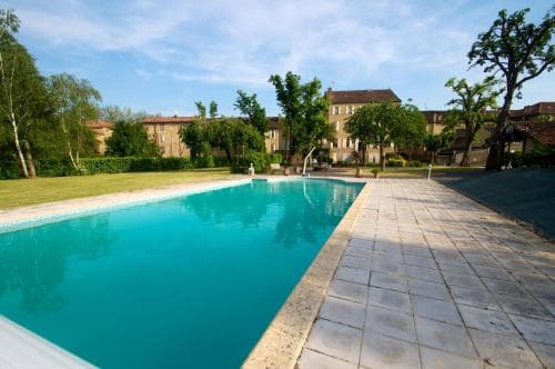 A serene outdoor swimming pool surrounded by lush greenery and traditional buildings invites relaxation, ideal for travelers seeking a tranquil resort experience.