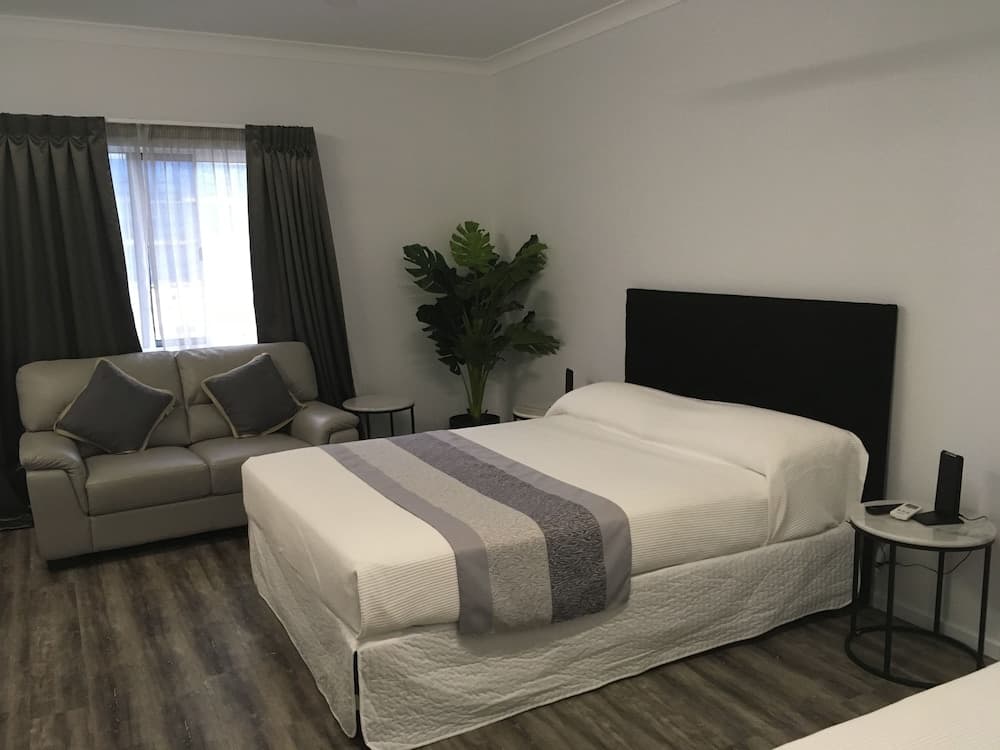 A cozy hotel room features a neatly made bed with white linens, a comfortable sofa by the window, a lush green plant, and modern furnishings, ideal for travelers seeking relaxation and comfort.