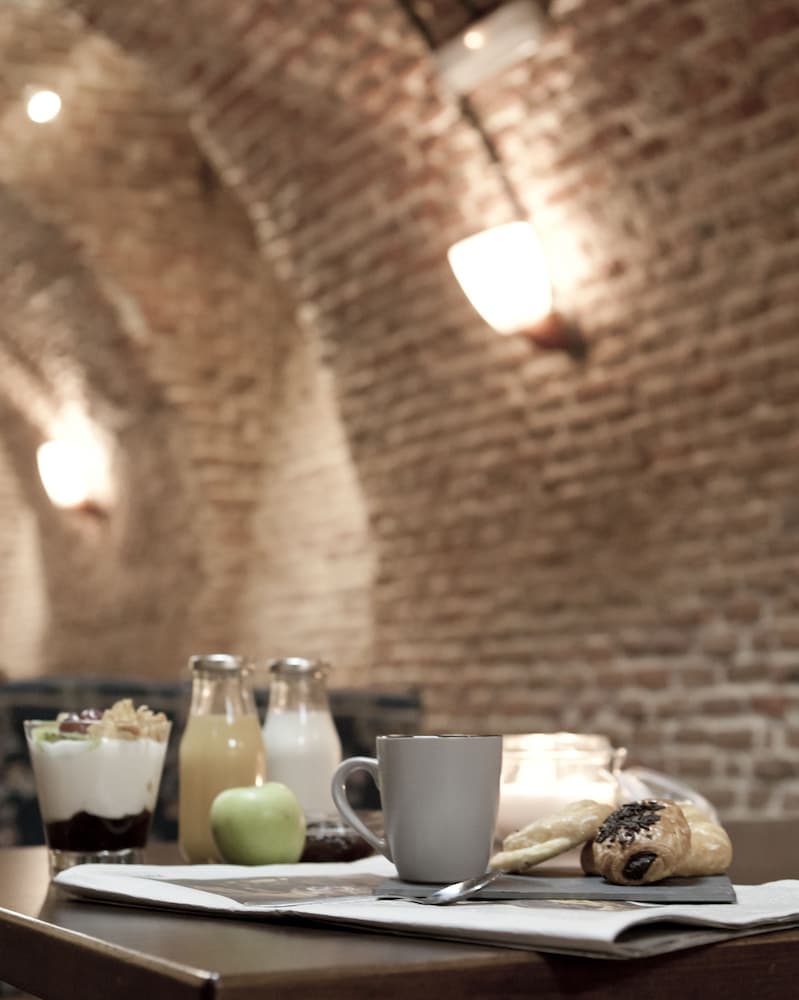 A cozy café scene with rustic brick walls, warm lighting, and a table set with coffee, pastries, yogurt, fruit, and newspapers, ideal for a relaxing breakfast or brunch outing.