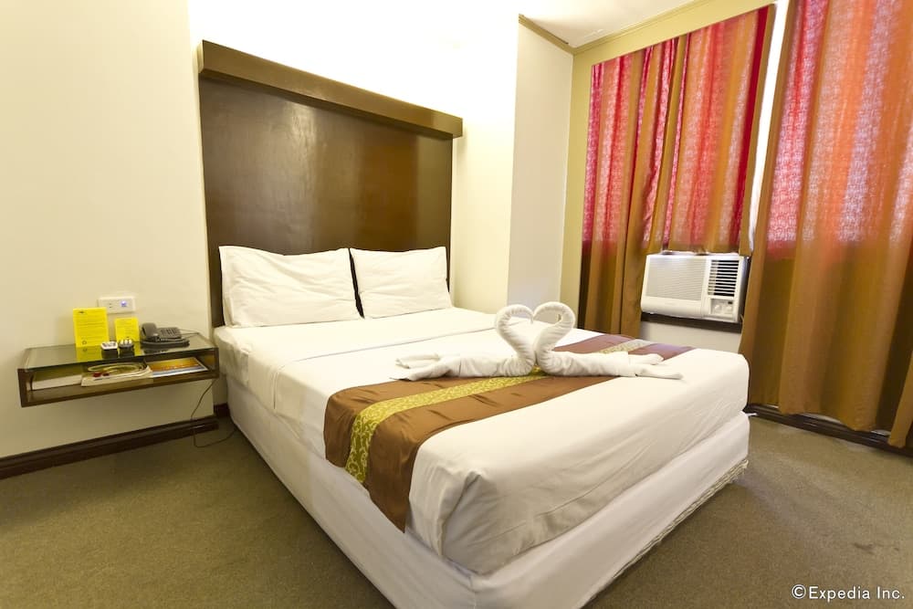 A cozy hotel room features a neatly made bed adorned with towel art, vibrant curtains, and a bedside table, ideal for travelers seeking comfort and relaxation.