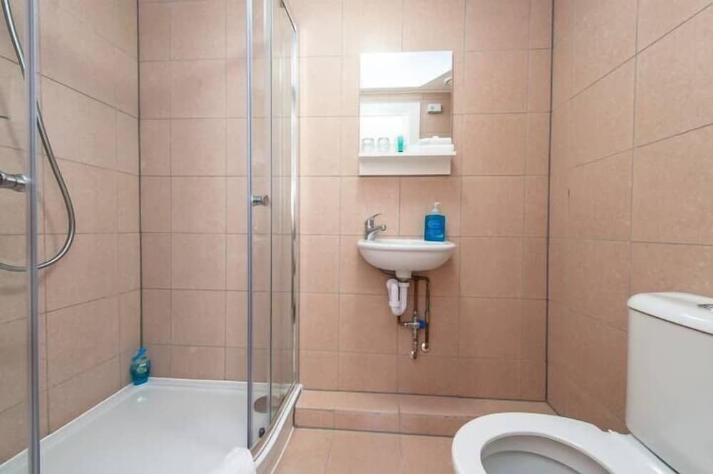 A compact bathroom with beige tiled walls features a glass-enclosed shower, a small sink with toiletries, and a toilet, ideal for travelers seeking efficient accommodation amenities.