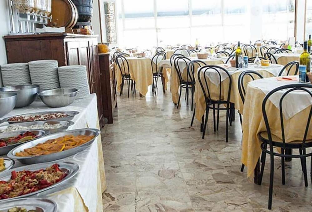 A spacious dining hall with marble floors, neatly arranged tables draped in yellow cloths, and a buffet line filled with colorful dishes invites travelers seeking a cozy and inviting meal experience.