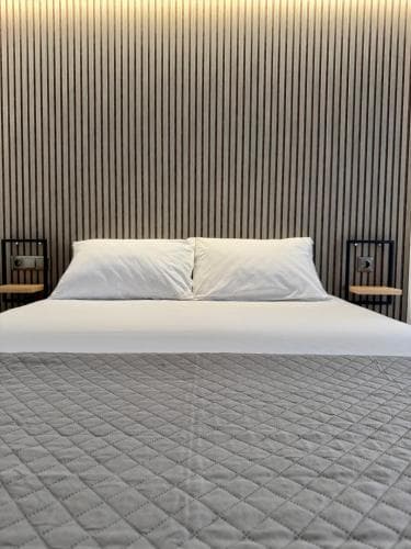 A cozy hotel room features a neatly made bed with white pillows against a textured wooden wall, exuding a modern and serene ambiance ideal for travelers seeking relaxation.
