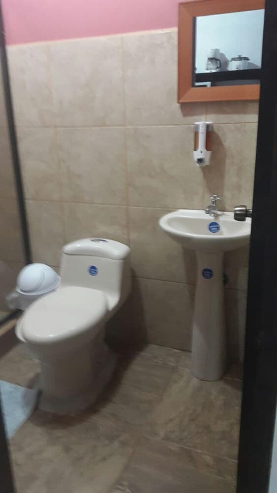 A compact bathroom with beige tiles, a toilet, pedestal sink, soap dispenser, and mirror reflects a clean and functional space ideal for travelers seeking basic amenities.