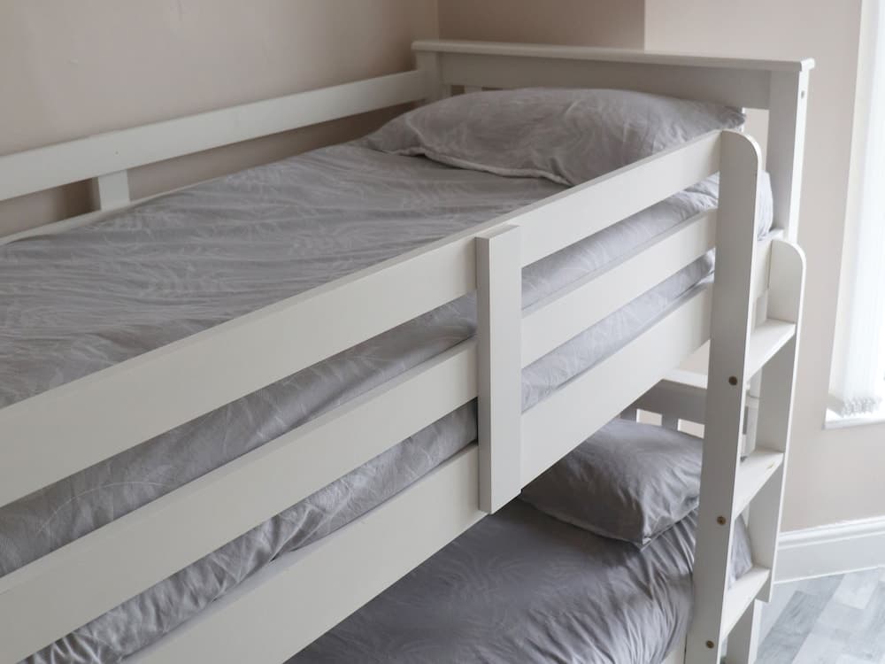 A cozy, minimalist bedroom features a white bunk bed with gray linens, ideal for travelers seeking comfortable accommodations in a shared space.