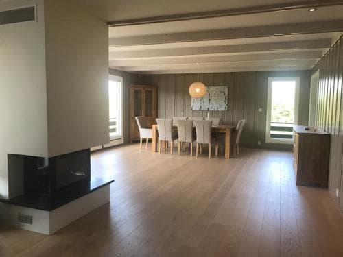 A cozy, spacious living room with wooden floors, a modern fireplace, and a dining area bathed in natural light from large windows, ideal for a relaxing family retreat or vacation rental.