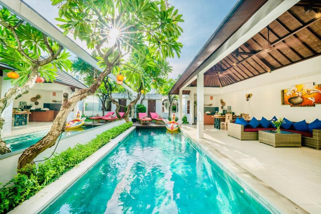 A serene tropical villa features a sparkling pool lined with lush greenery and vibrant lounge areas, ideal for a relaxing vacation retreat.