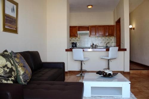 A cozy apartment interior features a modern kitchenette with wooden cabinets, a sleek living area with a plush sofa adorned with patterned cushions, and a minimalist coffee table, ideal for travelers seeking a comfortable and stylish short-term stay.