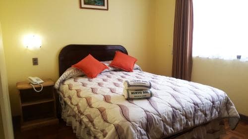 A cozy hotel room features a neatly made bed adorned with red pillows and a quilted coverlet, set against warm yellow walls and natural light filtering through sheer curtains, ideal for travelers seeking comfort and simplicity.