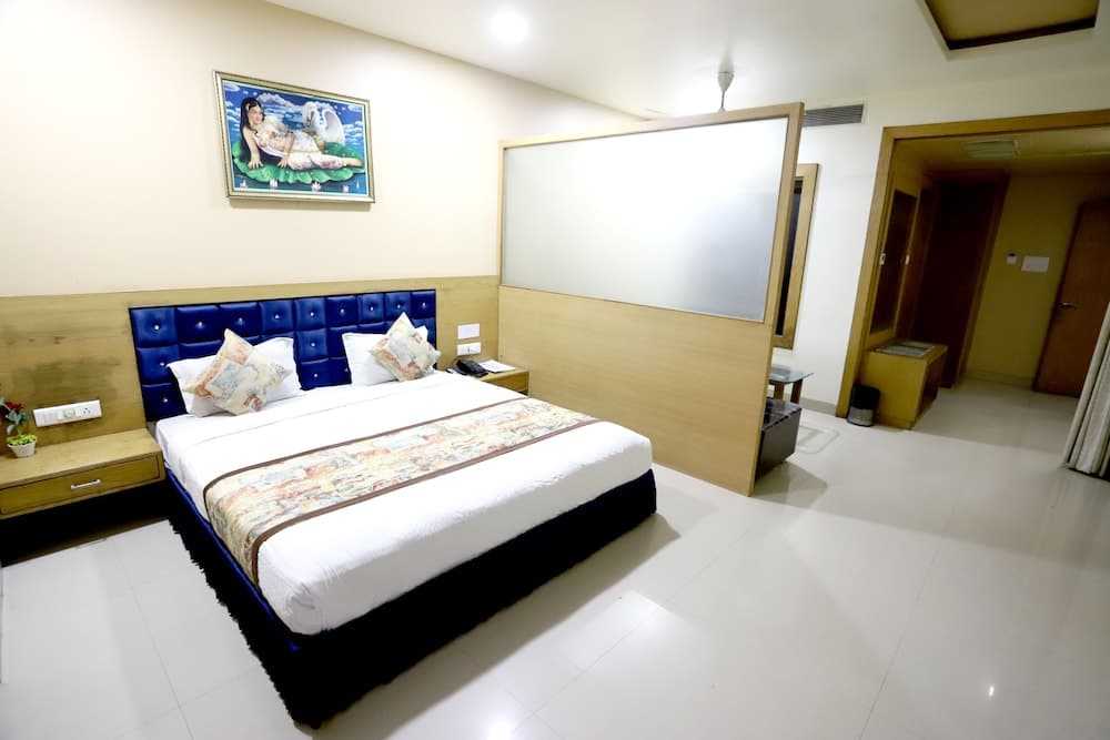 A cozy hotel room features a neatly made bed with a blue tufted headboard, a whimsical wall painting, and a minimalist design, ideal for travelers seeking comfort and simplicity.