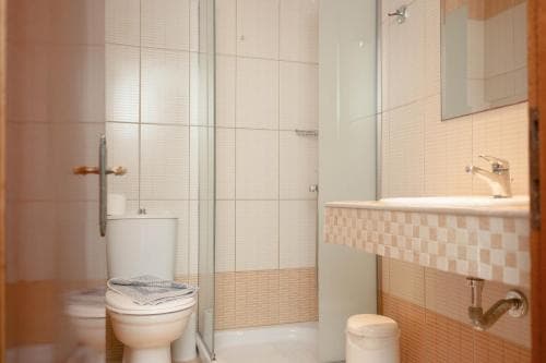A cozy hotel bathroom features tiled walls, a glass shower enclosure, a toilet with a towel draped over it, and a sink with a checkered backsplash, ideal for travelers seeking comfort and cleanliness.