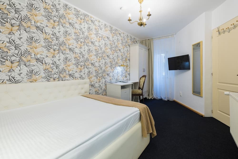 A cozy hotel room features a floral-patterned accent wall, elegant chandelier, and modern amenities like a flat-screen TV, ideal for travelers seeking comfort and style.