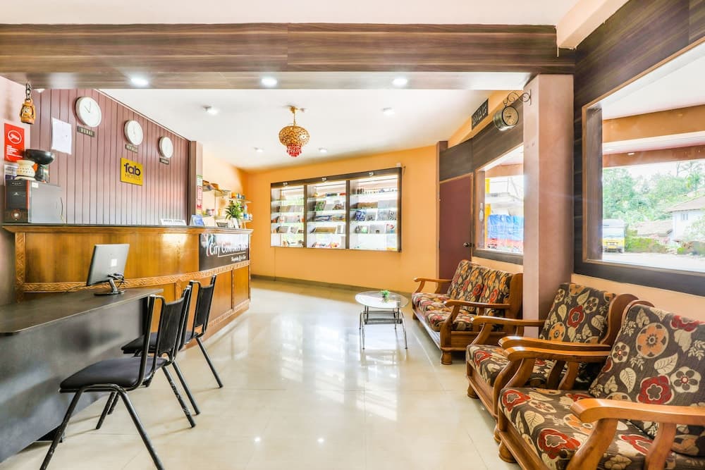 A cozy hotel lobby features a reception desk adorned with clocks and signage, floral-patterned sofas, a glass display cabinet, and a warm ambiance ideal for travelers seeking comfort and convenience.
