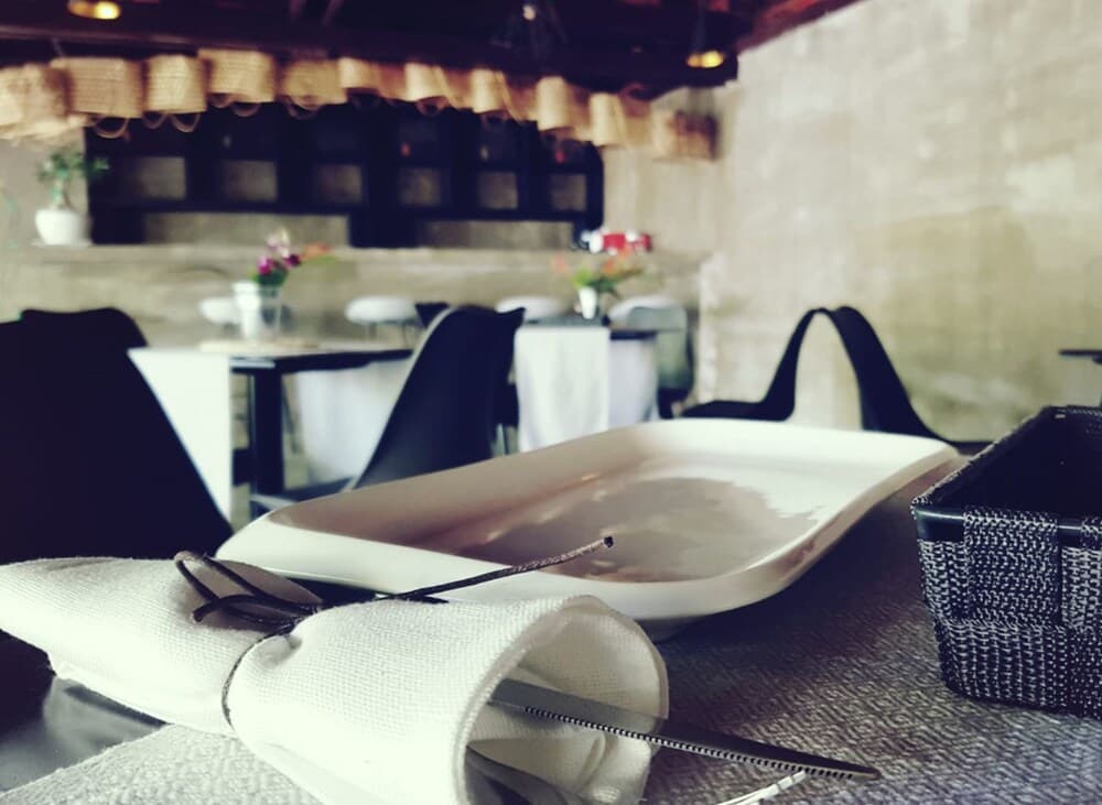 A cozy restaurant setting with rustic charm features a neatly arranged table, white plates, cutlery wrapped in napkins, and woven baskets, ideal for travelers seeking a serene dining experience.