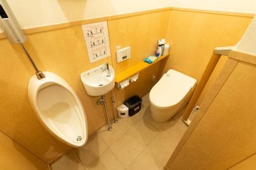 A clean and organized restroom featuring a toilet, urinal, sink, and various amenities, ideal for travelers seeking hygiene facilities in public spaces.