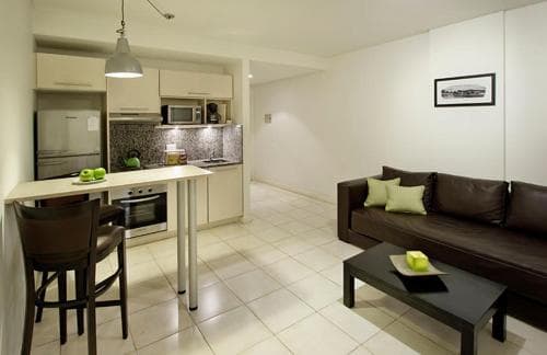 A cozy apartment interior features a modern kitchenette with white cabinets, a sleek dining area, and a comfortable living space with a brown sofa, ideal for travelers seeking a compact yet stylish accommodation.