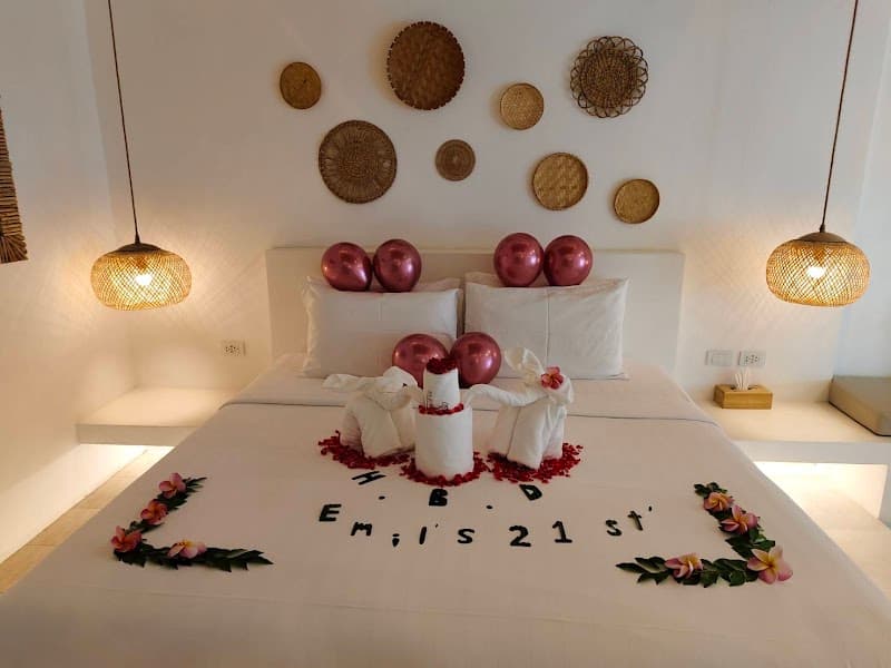 A cozy resort bedroom at Elephant Beach Club & Resort Samui features a beautifully decorated bed with balloons, flowers, and personalized letters spelling "Emil's 21st," creating an intimate and celebratory atmosphere ideal for special occasions.