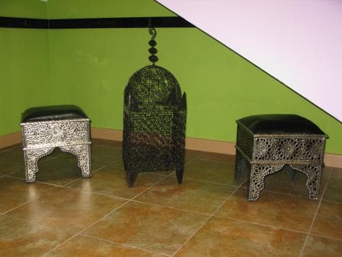An intricately designed Moroccan-style seating area with ornate metal stools and a central chair set against a vibrant green wall, evoking a serene and exotic ambiance ideal for cultural exploration or interior design inspiration.