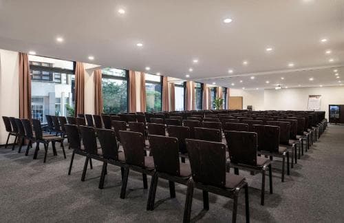 A spacious conference room with rows of chairs, large windows, and warm lighting creates an inviting atmosphere ideal for professional gatherings and business meetings.