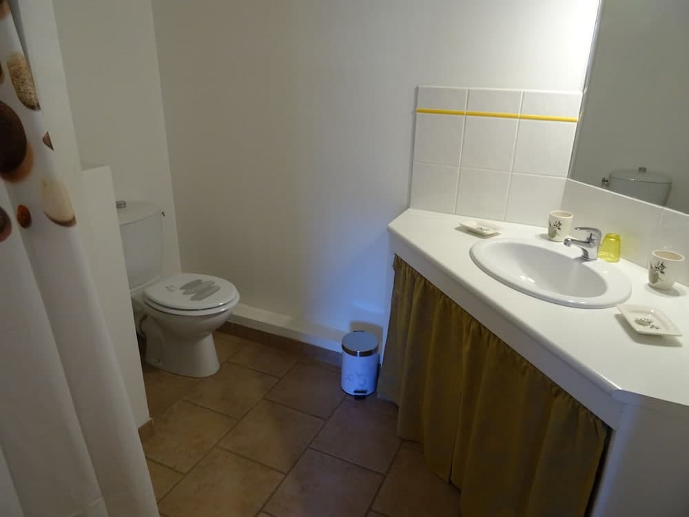 A cozy bathroom with tiled walls, a sink adorned with cups and toiletries, a toilet, and a shower curtain featuring seashell patterns, ideal for travelers seeking a clean and functional accommodation space.