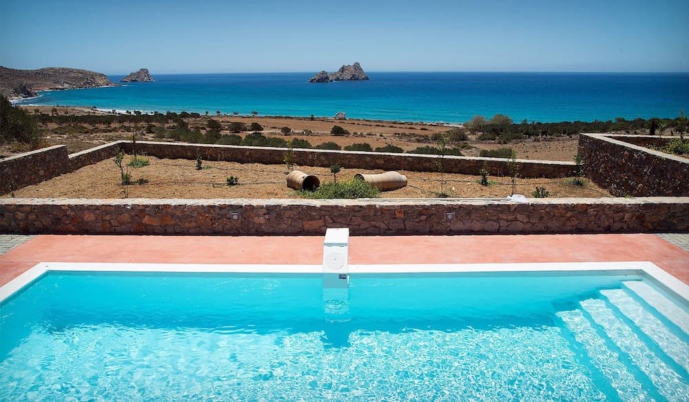 A serene coastal retreat features a crystal-clear pool overlooking the turquoise sea and rugged cliffs, ideal for luxury relaxation and scenic photography.