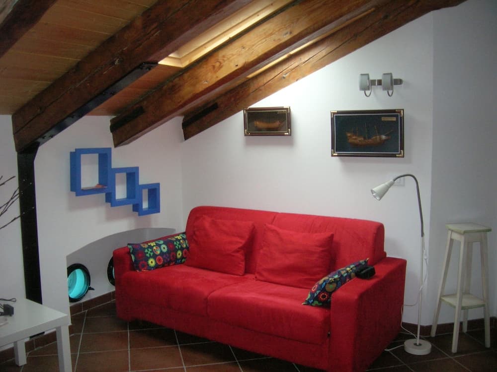 A cozy attic living space features a vibrant red sofa under wooden beams, adorned with nautical-themed artwork and modern furnishings, ideal for travelers seeking a charming and intimate accommodation.