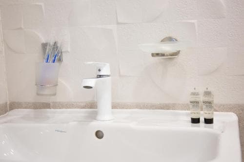 A clean hotel bathroom sink area features a modern faucet, toiletries, and a textured wall, ideal for travelers seeking basic amenities in a budget-friendly accommodation.