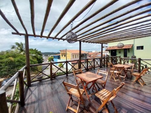 A cozy wooden rooftop terrace with bamboo pergola and hanging lanterns offers scenic views of colorful houses and lush greenery, perfect for travelers seeking relaxation and social gatherings in a tropical setting.