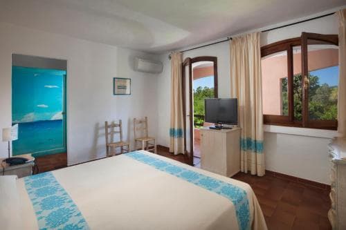 A cozy hotel room with a neatly made bed, vibrant blue accents, and large windows offering a serene view of lush greenery, ideal for travelers seeking relaxation and comfort.