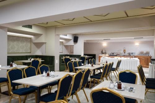 A cozy hotel dining area features neatly arranged tables with blue chairs under warm lighting, ideal for travelers seeking a comfortable breakfast or casual meal setting.