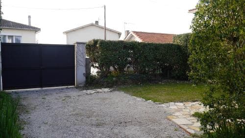 A serene suburban garden with a gravel driveway, stone path, lush greenery, and a black gate invites travelers seeking a peaceful residential retreat.