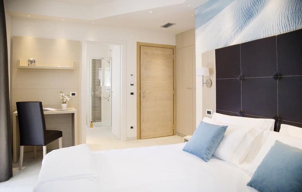 A serene hotel room features a cozy bed with blue accents, a modern desk setup, and a visible bathroom, ideal for travelers seeking comfort and relaxation.