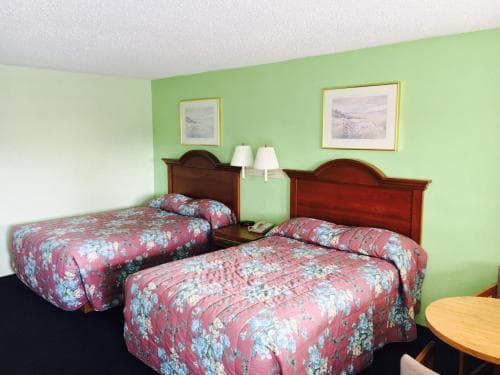 A cozy motel room features two floral-patterned beds against a green wall, framed by simple artwork, creating a welcoming atmosphere ideal for budget travelers seeking comfort.