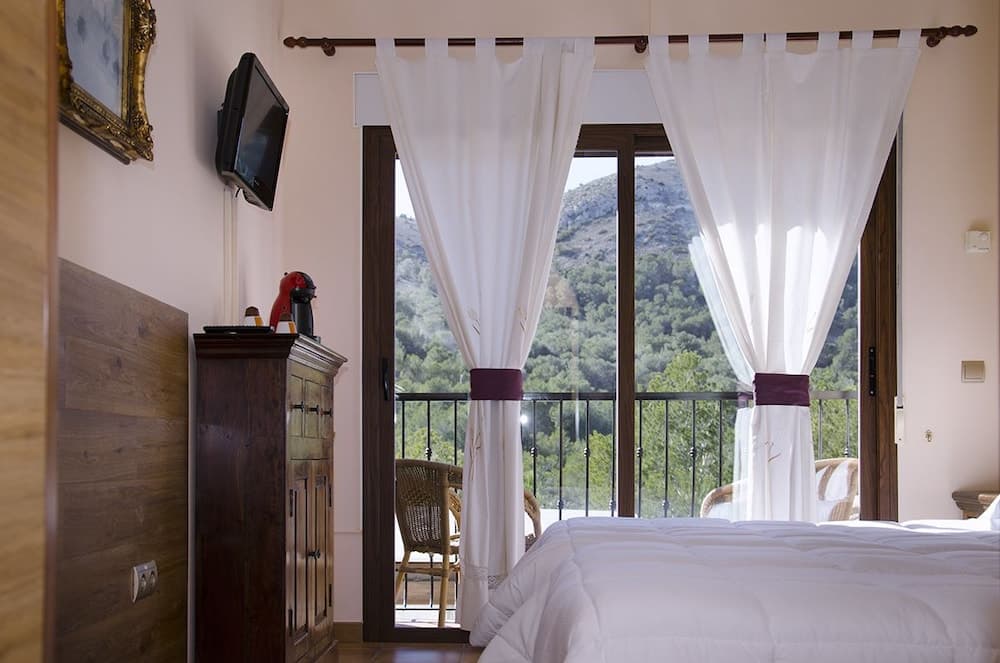 A cozy bedroom with elegant white curtains frames a serene mountain view, perfect for travelers seeking relaxation in a tranquil retreat.